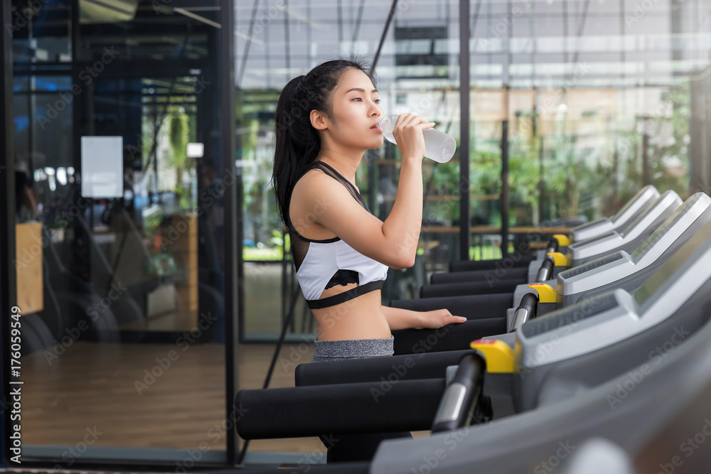 Fitness woman drinking water from bottle after run on running machine