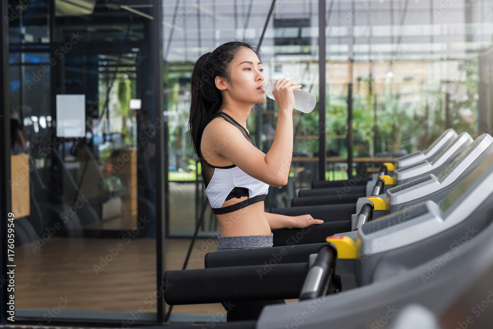 Fitness woman drinking water from bottle after run on running machine Fitness woman drinking water from bottle after run on running machine