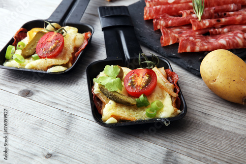 Delicious traditional Swiss melted raclette cheese on diced boiled or baked potato served in individual skillets with salami..