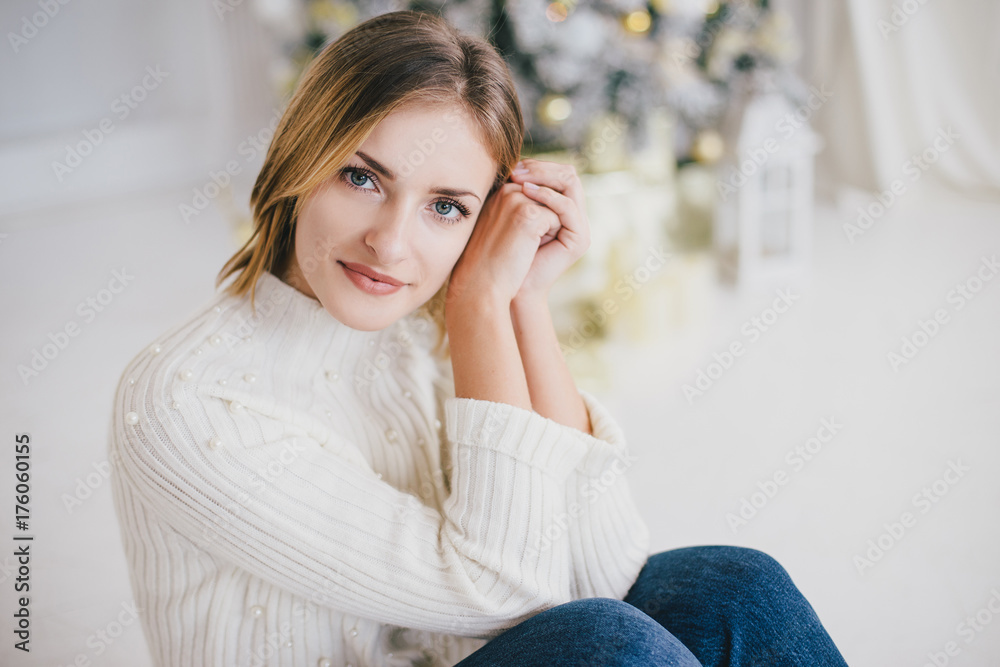 Naklejka premium Beautiful young woman posing under Christmas tree in a holiday interior