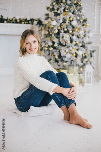 Beautiful young woman posing under Christmas tree in a holiday interior