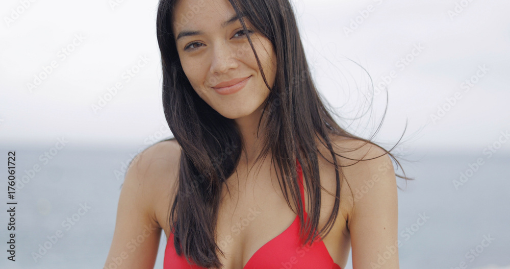 Portrait of adorable ethnic model in red swimsuit looking at camera with calm expression on background of romantic sea. Portrait of adorable ethnic model in red swimsuit looking at camera with calm expression on background of romantic sea.