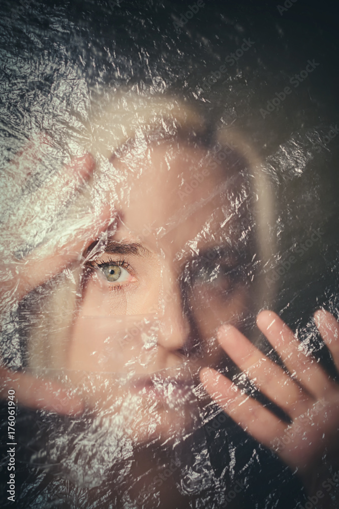 Woman looking scared through hole in transparent plastic curtain, scared and alone in dark