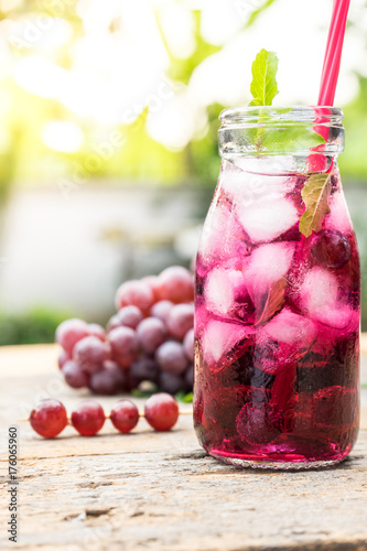 cool grape juice in glass jar on old wood with tree background. fresh drink and healthy concept