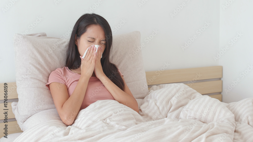 Woman sneezing on bed Woman sneezing on bed