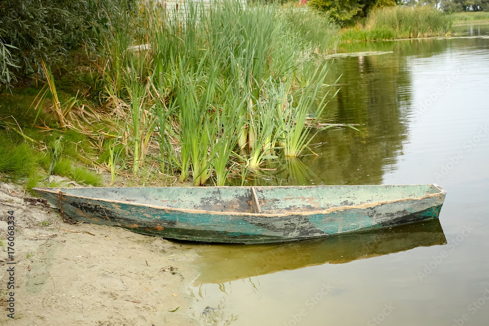 old wooden boat on the shore of a small pond, river or lake in the afternoon. old wooden boat on the shore of a small pond, river or lake in the afternoon.