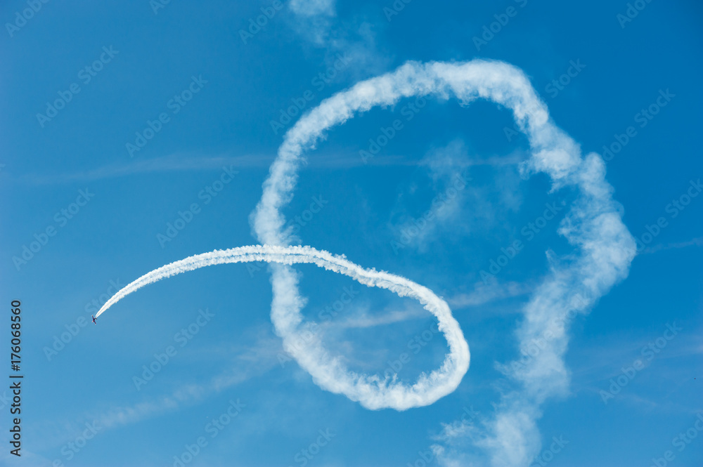 Naklejka premium Plane doing acrobatics in blue sky and drawing curves with white smoke