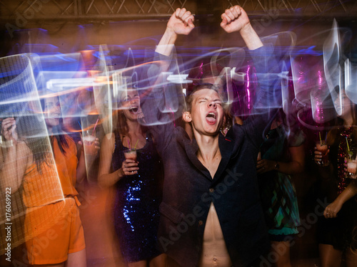 Active happy male on dance floor in motion. Joyful New Year in night club, positive Christmas celebration. Disco party in blurred colors, modern youth life