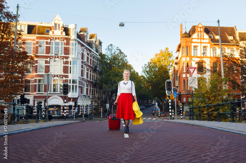 The woman with suitcase is walking in the street of Amsterdam city in autumn
