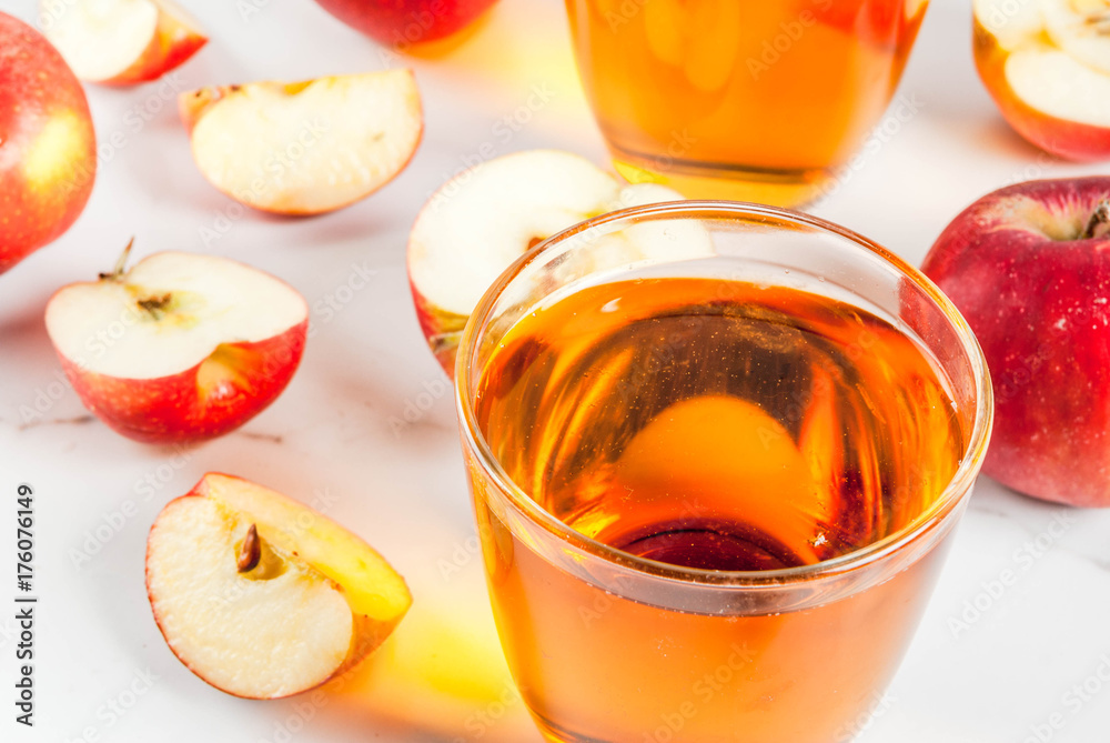 Fresh organic farm apple juice in glasses with raw whole and sliced red apples, on white marble table, copy space Fresh organic farm apple juice in glasses with raw whole and sliced red apples, on white marble table, copy space