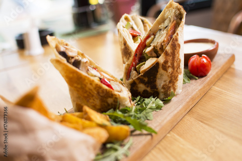 Burrito with grilled chicken and vegetables. Shawarma from juicy beef, lettuce, tomatoes, cucumbers, paprika and onion in pita bread.