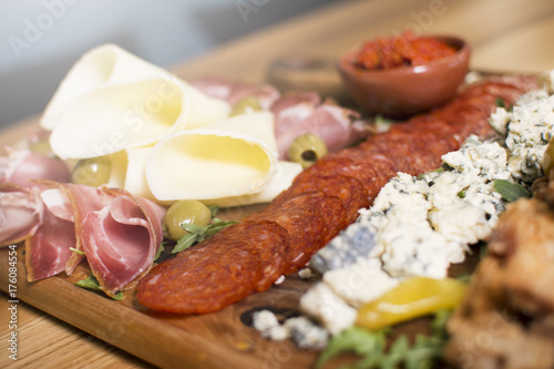 Mediterranean olives, sun-dried tomatoes, baguette slices, camembert cheese and spices on wooden background. Sausage and prosciutto slices on a wooden board. Appetizers served at an event.