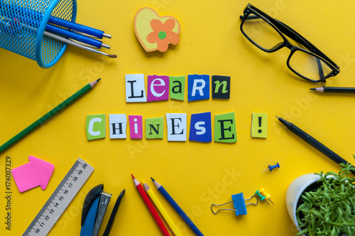 Word LEARN CHINESE made with carved letters on yellow desk with office or school supplies, stationery. Concept of chinese language courses