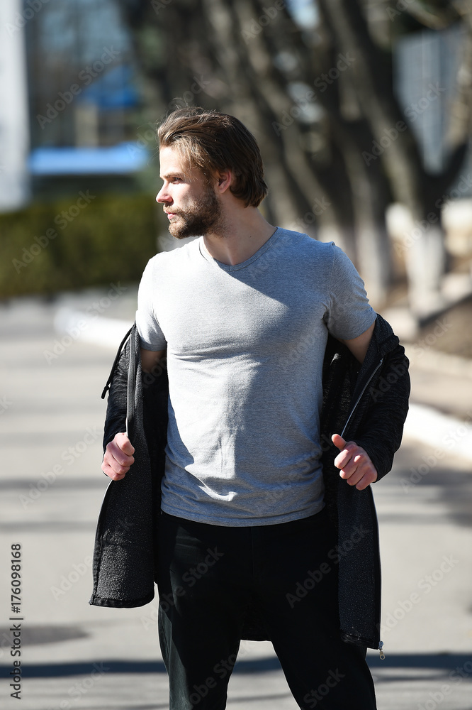 Fototapeta premium Guy with beard and haircut in grey tshirt undressing coat