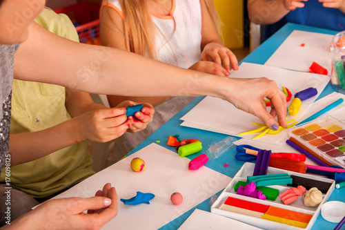 Plasticine modeling clay in children class. Teacher teaches kids together play dough and mold from plasticine in kindergarten or preschool. Group of four people. They learn to live in a team.