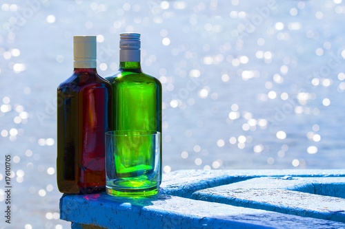 Bottles of whiskey and gin with glass on background of lake