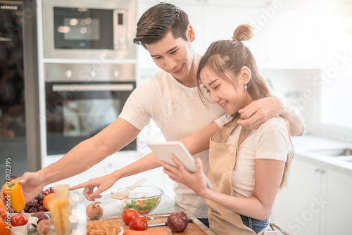 happy young couple cooking together in the kitchen at home. looking at tablet pc.