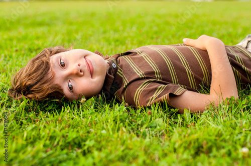 Pensive little boy lies on a lawn photo