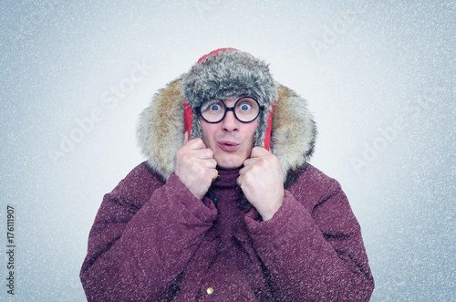 Frozen man in glasses and winter clothes warming ears, cold, snow, blizzard