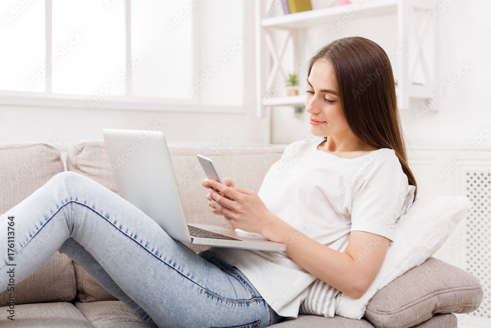 Young woman using smatrphone with laptop at home on the couch. Young woman using smatrphone with laptop at home on the couch.