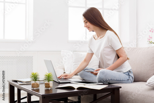 Pretty girl typing on laptop at home on the couch. Dark-haired girl in casual