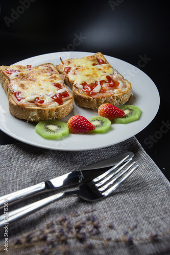 warm toast with bacon and melted mozzarella cheese on dark background