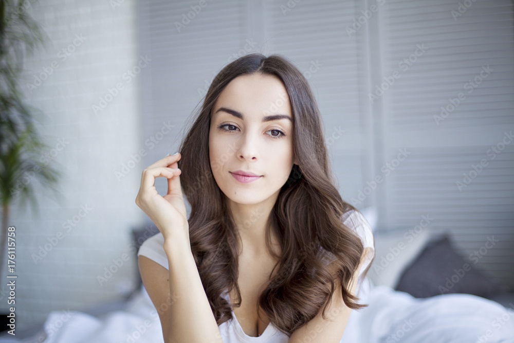 Beautiful young brunette woman sitting at the end of the white bed. Beautiful young brunette woman sitting at the end of the white bed.