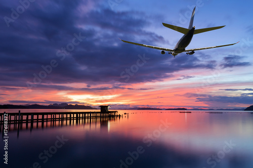 Commercial airplane flying above clouds with dramatic sunset or sunrise sky and light background.