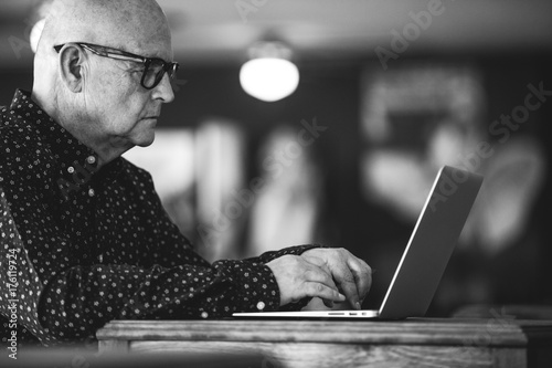 Stylish senior man, wearing glasses and working with a laptop in a business office in black and white photo