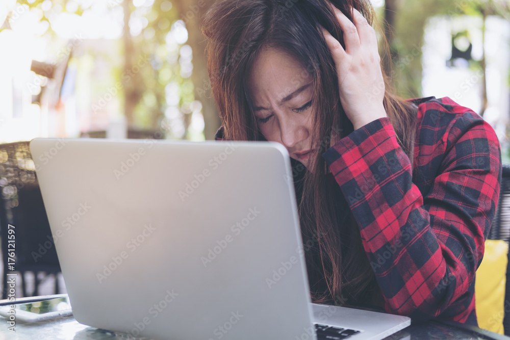 Closeup image of an Asian business woman with feeling stressed and tired , close her eyes while using laptop on glass table sitting at outdoor with green nature background Closeup image of an Asian business woman with feeling stressed and tired , close her eyes while using laptop on glass table sitting at outdoor with green nature background