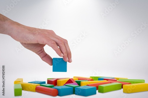 Composite image of cropped hand arranging colorful blocks