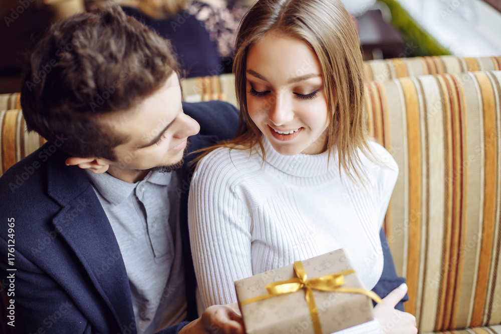The young man gives a gift to his beloved woman at the coffee shop - the concept of happiness, relationships and celebration The young man gives a gift to his beloved woman at the coffee shop - the concept of happiness, relationships and celebration