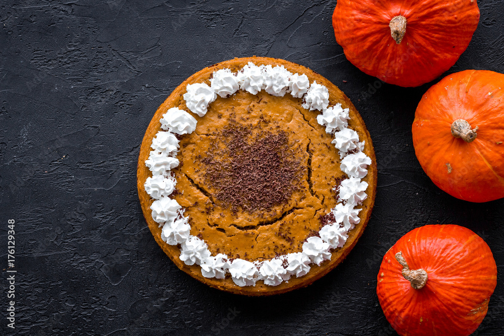Homemade pumpkin pie decorated whipped cream and chocolate near pumpkins on black background top view copyspace Homemade pumpkin pie decorated whipped cream and chocolate near pumpkins on black background top view copyspace