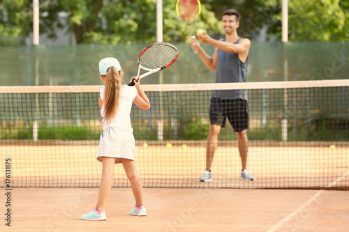 Young trainer with little girl playing tennis on court