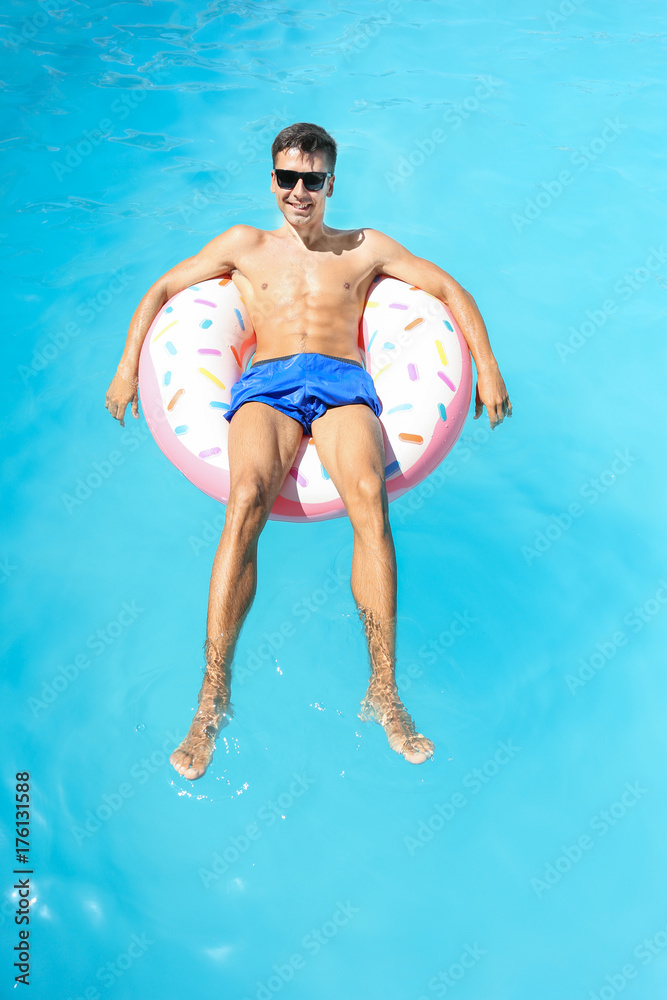 Young man relaxing on inflatable donut in swimming pool