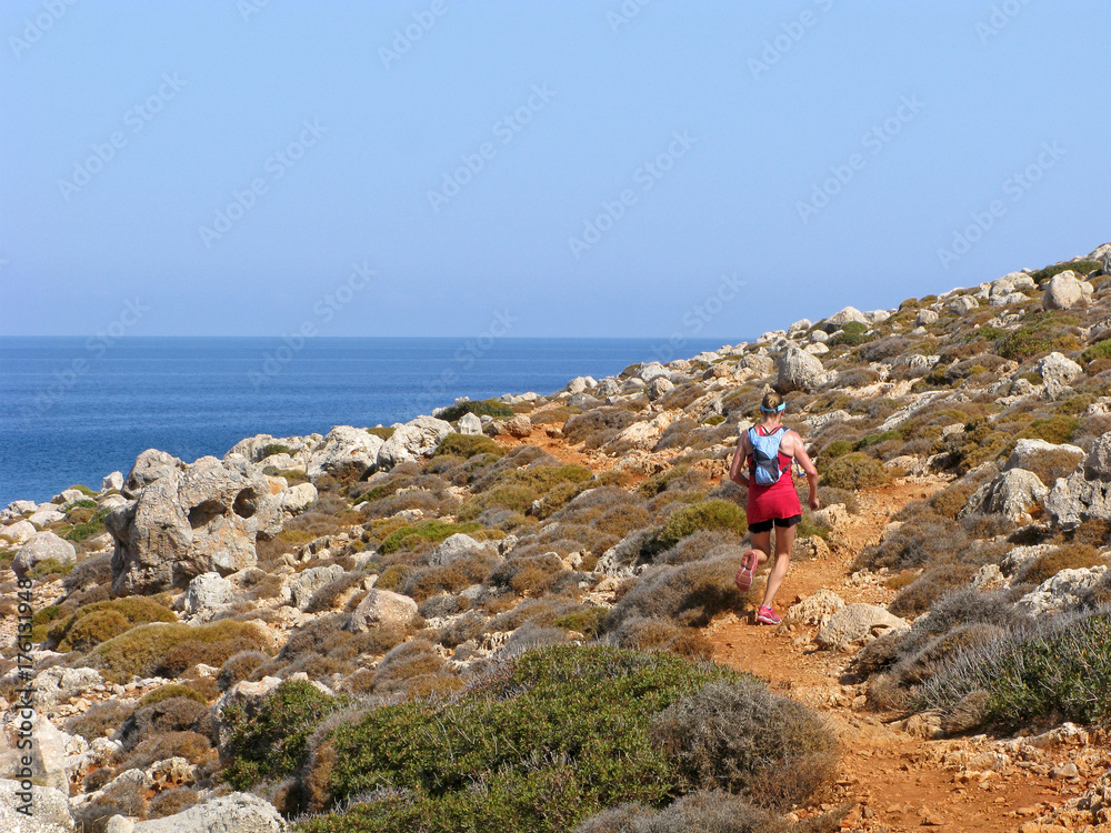 Woman runs on rocky coast. Sunny day, clear sky, blue sea.