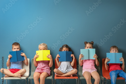 Cute little children reading books while sitting near color wall © Africa Studio