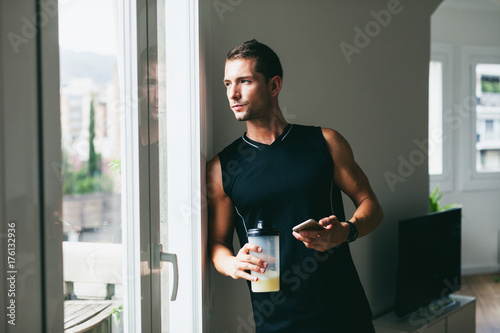 Young man using his phone whilst drinking a protein shake after hard workout. photo