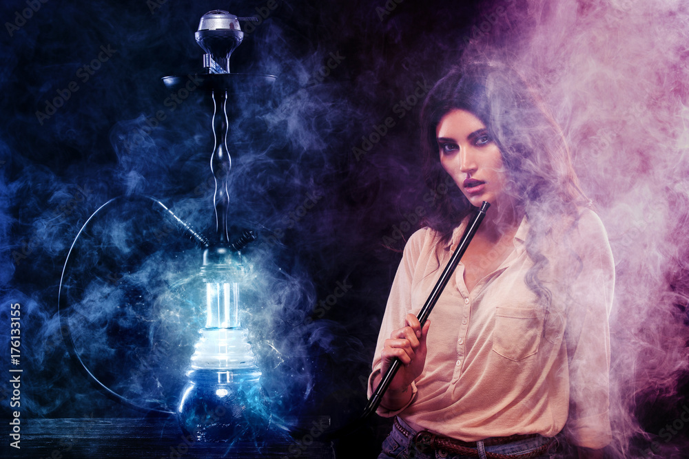 Young, beautiful woman in the night club or bar smoke a hookah. The