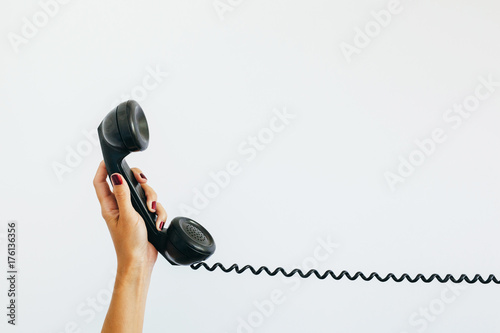 woman's hand holding a vintage telephone  with cord stretched out photo