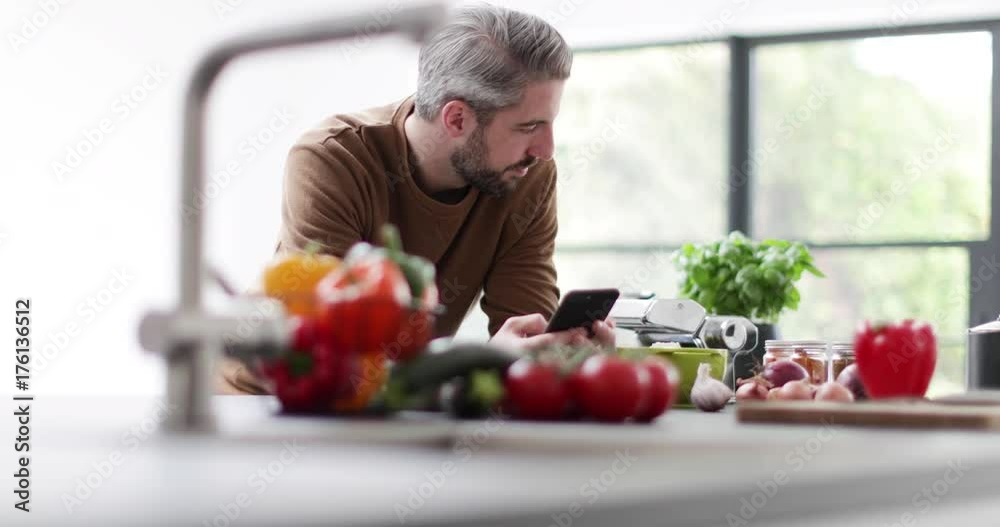 Adult male looking up recipe on smartphone in kitchen Adult male looking up recipe on smartphone in kitchen