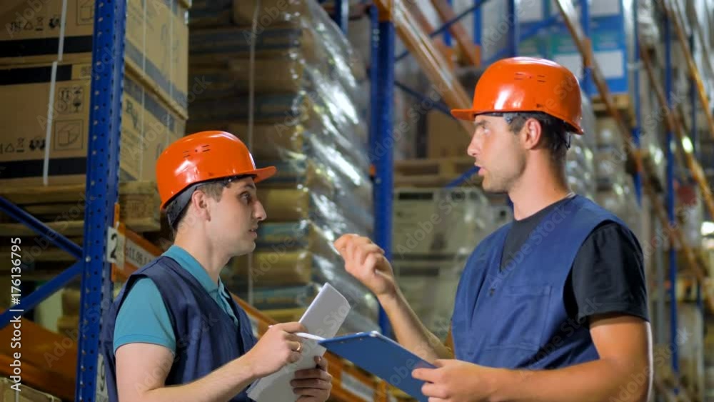 Two warehouse workers point and discuss storage items. Two warehouse workers point and discuss storage items.