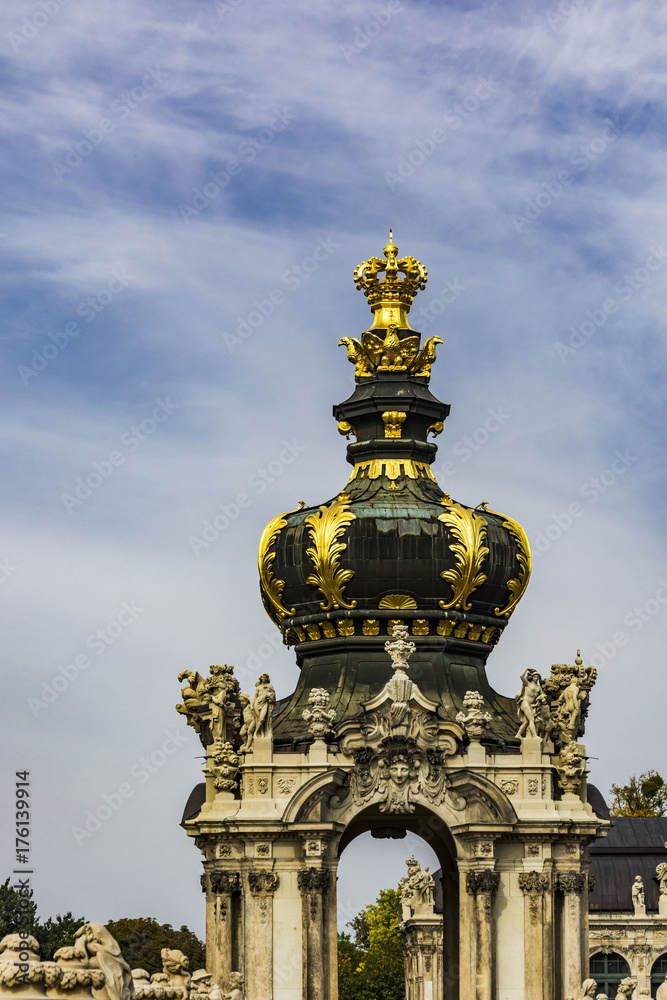 Gold ornaments on tower dome of monument building under blue sky.