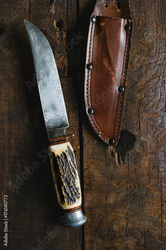 Old hunting knife with leather sheath on wood background.