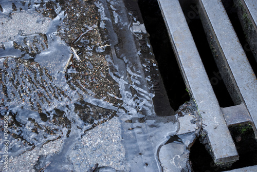 Wasser / Regenwasser fliesst durch Kanaldeckel in Kanalisation 