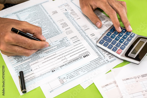 man filling tax form with pen, calculator