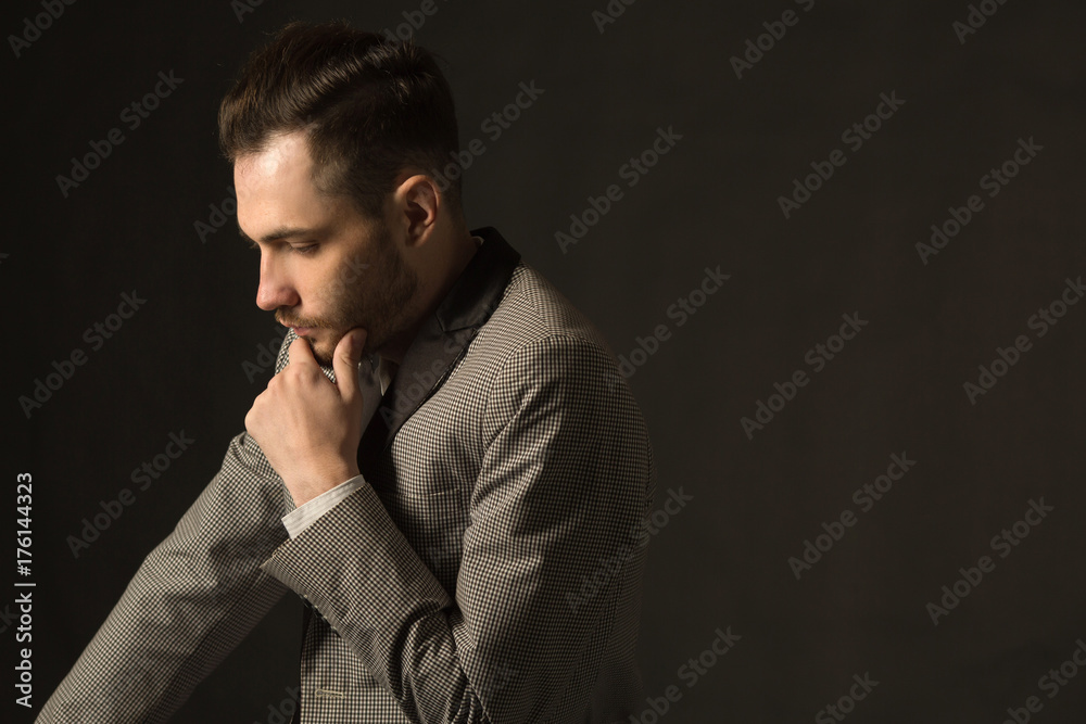 young serious man with an unshaven face in a suit with a pensive face on a dark background