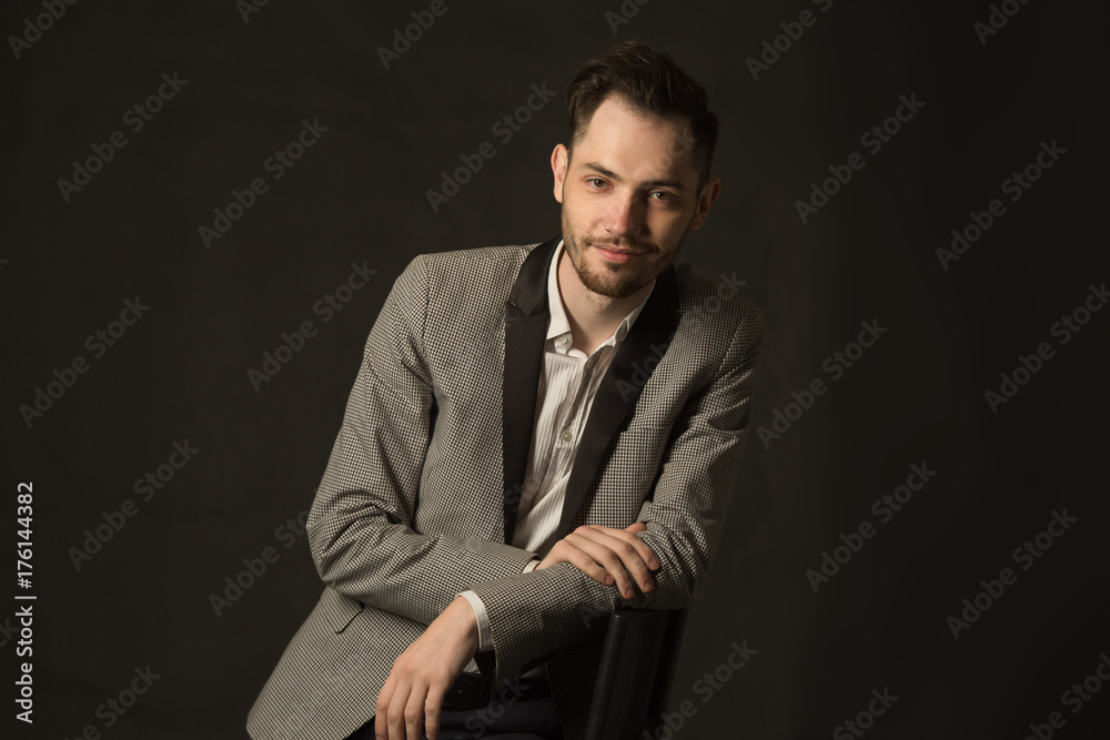 portrait of a young man with an unshaven face in a suit with a smile on a dark background portrait of a young man with an unshaven face in a suit with a smile on a dark background