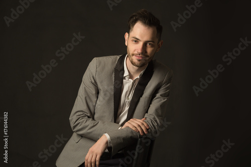 portrait of a young man with an unshaven face in a suit with a smile on a dark background © Alexandr