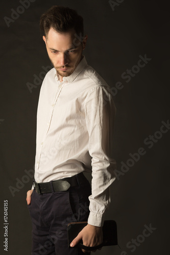 young man with unshaven face on white shirt on dark background © Alexandr